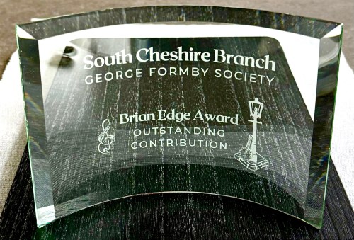 A photograph of the Brian Edge Award. It is curved glass stating: "South Cheshire Branch, George Formby Society. Brian Edge Award, Outstanding Contribution."